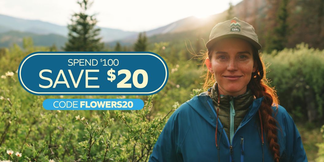 A woman stands in an alpine area with the sun setting behind her. Text overlay reads: Spend $100 Save $20 Code FLOWERS20