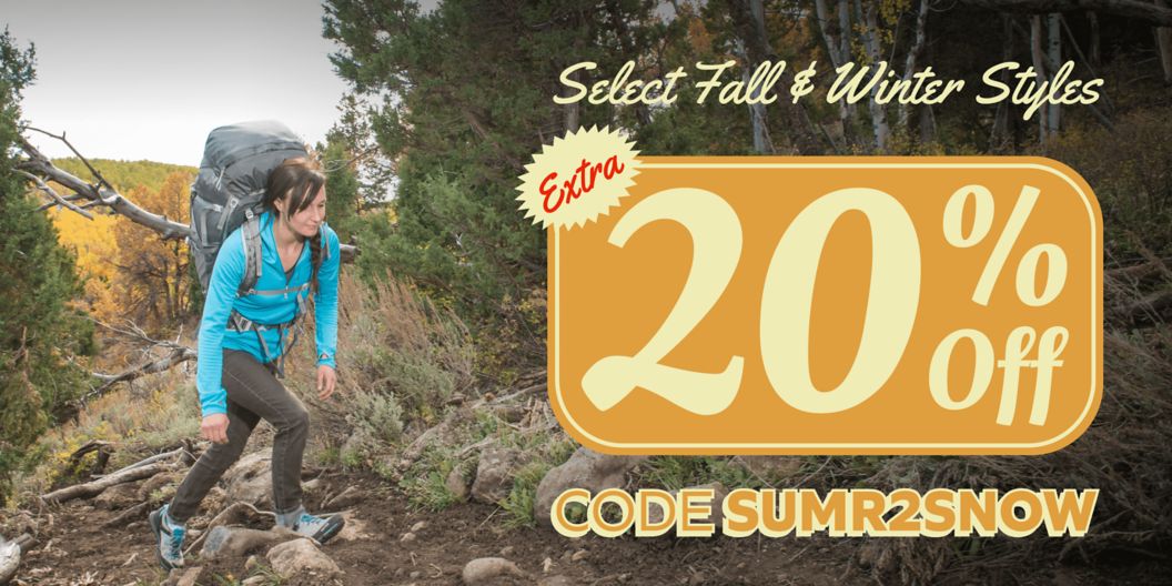 A woman backpacks through forest. Text overlay reads: Select fall & winter styles extra 20% off code SUMR2SNOW. 