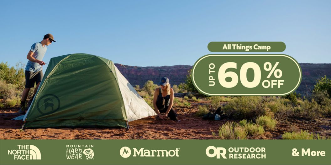 Two people set up a tent in the desert. Text overlay reads All Things Camp, up to 60% off. Brand logos at bottom read: The North Face, Mountain Hardwear, Marmot, Outdoor Research & More.