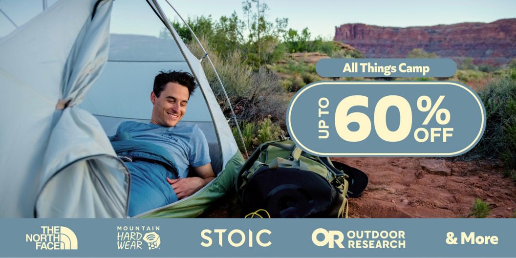 A smiling man laying in a tent in the desert. Text reads “All things camp, up to 60% off.” Below are brand logos for The North Face, Mountain Hardware, Stoic, and Outdoor Research.    