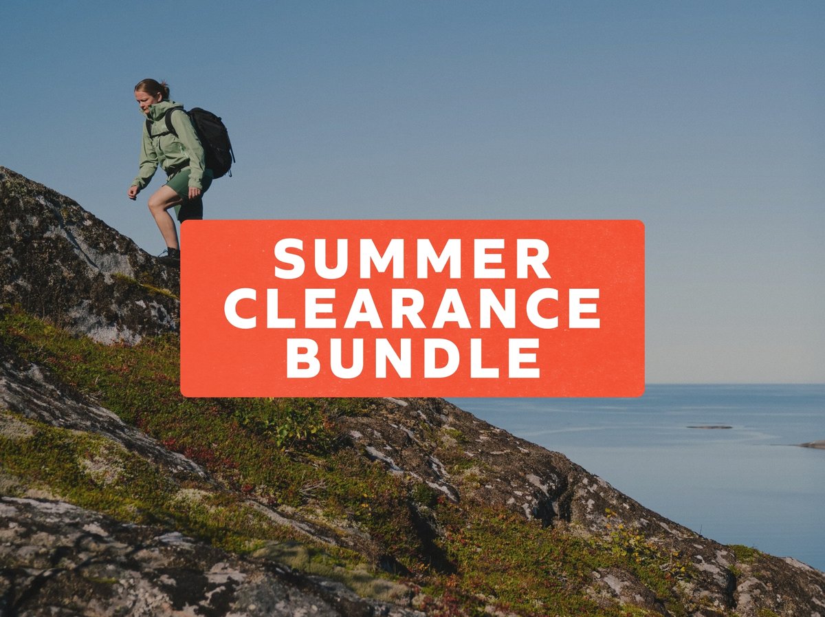 Summer Clearance Bundle — hiker with a backpack descending a mossy coastal ridge above calm blue water.
