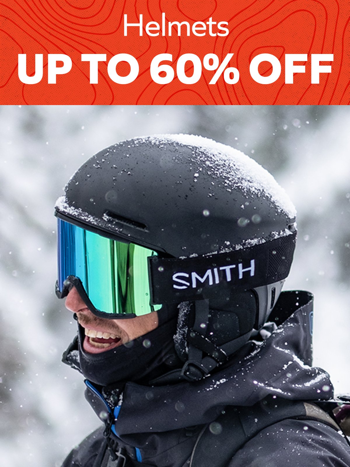 Helmets up to 60% off — smiling skier in a snow-covered black Smith helmet and mirrored goggles during a snowfall.