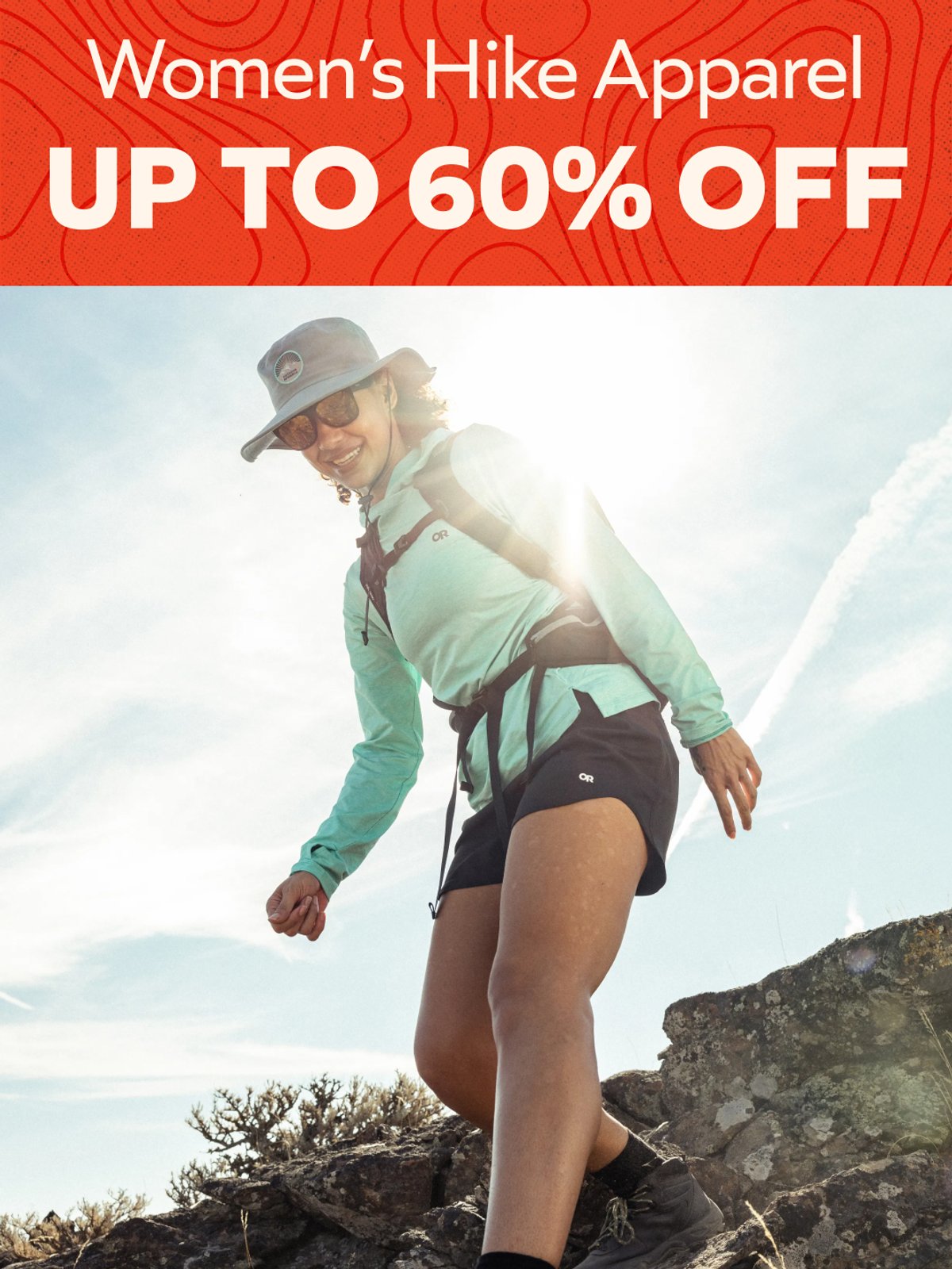 Up to 60% off Women's Hike Apparel — woman in turquoise jacket and shorts hiking on sunny rocky terrain